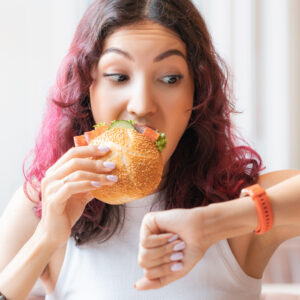 Young woman eating a sandwich and looking to the side at her watch