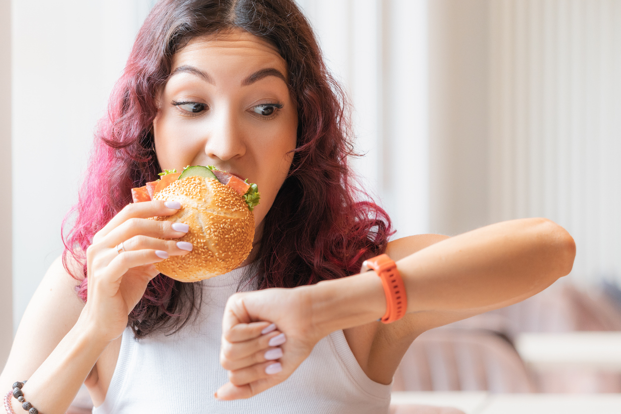 Young woman eating a sandwich and looking to the side at her watch