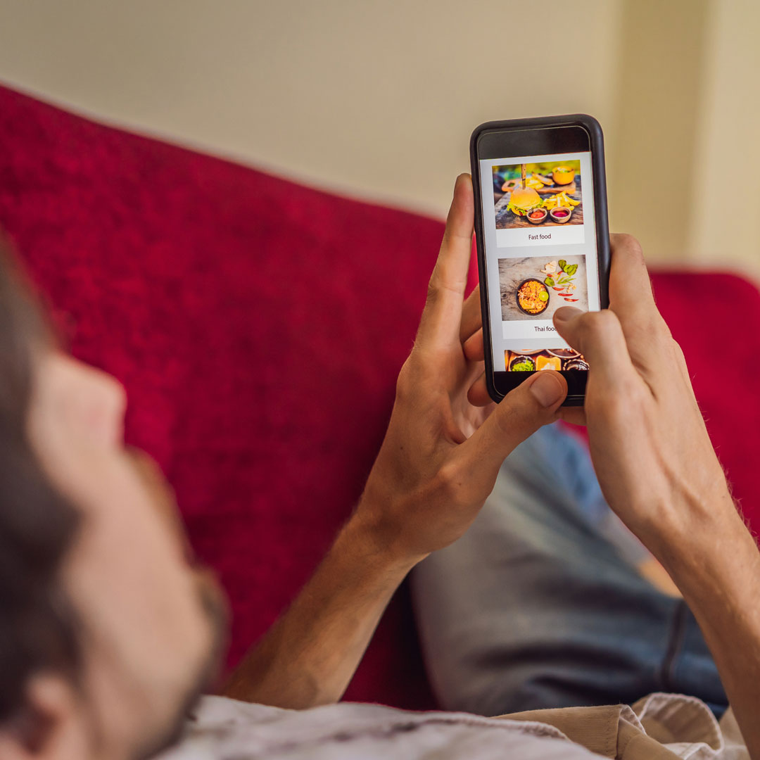 Man laying down on red couch surfing on mobile phone to figure out what to order for next meal .